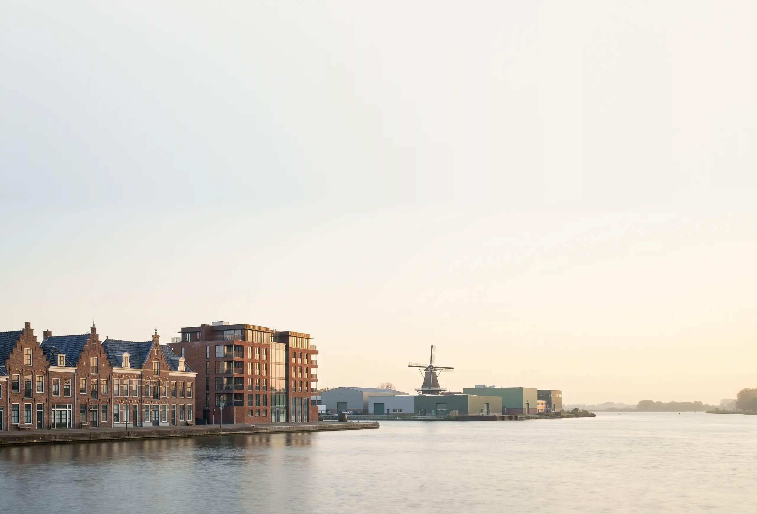 Hollandse waterkant met grachtenpanden, een modern kantoorgebouw, bedrijfshallen en een molen